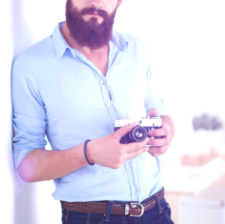 Young beard man holding a camera while standing against white background.の写真素材
