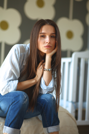 Young tired woman sitting on the bed near children's cot.の写真素材