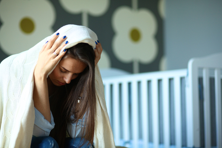 Young tired woman sitting on the bed near children's cot.の写真素材