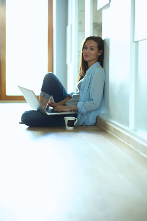 Young beautiful woman at home sitting on the floor with laptopの写真素材