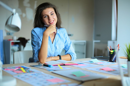 Young woman sitting at the desk with instruments, plan and laptopの写真素材
