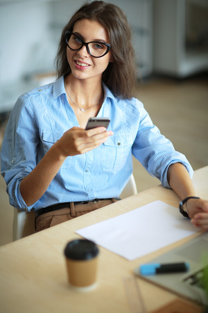 Beautiful young business woman sitting at office desk and talking on cell phoneの写真素材