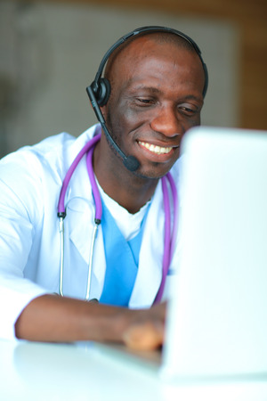 Portrait of young male doctor wearing headset while using computer at desk in clinicの写真素材