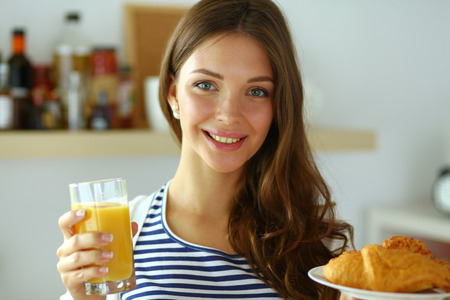Young woman with glass of juice and cakes standing in kitchen .の写真素材