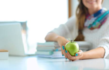 Female college students sitting on the desk with apple on a pile of booksの写真素材