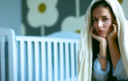 Young tired woman sitting on the bed near children's cot.の写真素材