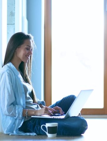 Young beautiful woman at home sitting on the floor with laptopの写真素材