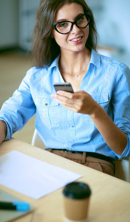 Beautiful young business woman sitting at office desk and talking on cell phoneの写真素材
