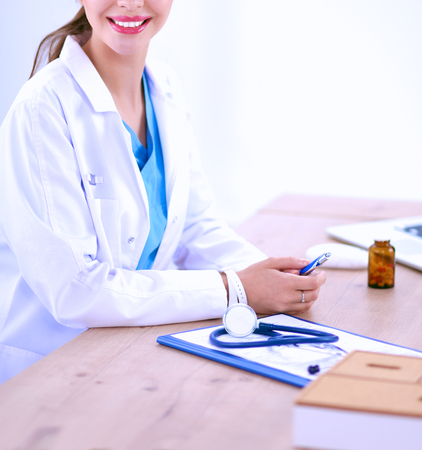 Beautiful young smiling female doctor sitting at the desk and writing.の写真素材