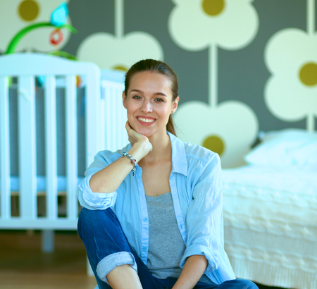 Young woman sitting on the floor near children's cot.の写真素材