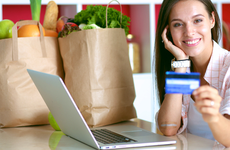 Smiling woman online shopping using tablet and credit card in kitchen.の写真素材