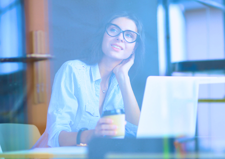 Young woman sitting at office table with laptop,view through windowの写真素材
