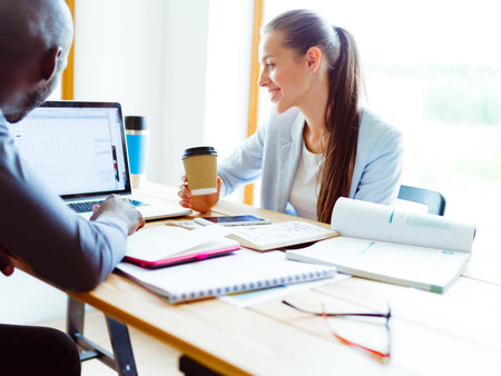 Attractive woman sitting at desk in office, working with laptop , having takeaway coffee