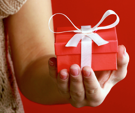 Female hand holding gift box isolated on red backgroundの写真素材