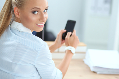 Businesswoman sending message with smartphone in officeの写真素材