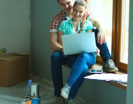Portrait of young couple moving in new home sitting with laptop..の写真素材