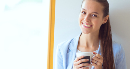 Attractive woman sitting at desk in office having takeaway coffee.の写真素材