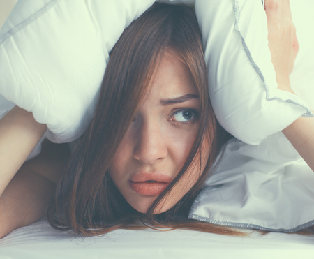 Female lying on bed and closing her ears with pillow.の写真素材