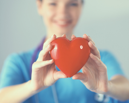 Young woman doctor holding a red heart, standing on grayの写真素材