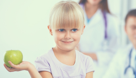 Child and medicine concept - female doctor giving an apple to little girl .の写真素材