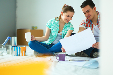 Man and woman looking at their house plans sitting in their new houseの写真素材