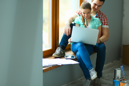 Portrait of young couple moving in new home sitting with laptopの写真素材