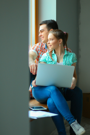Portrait of young couple moving in new home sitting with laptopの写真素材