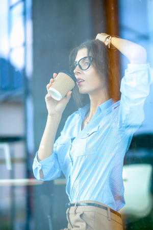 Cheerful businesswoman drinking from mug while working on laptop at the officeの写真素材