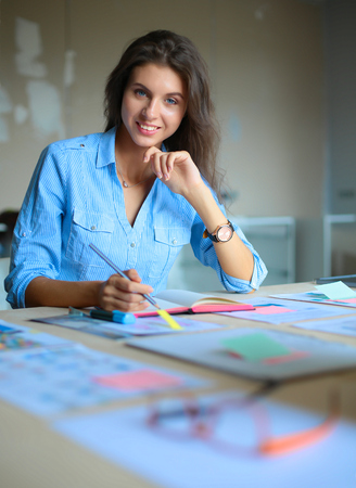 Young woman sitting at the desk with instruments, plan and laptopの写真素材