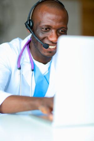 Portrait of young male doctor wearing headset while using computer at desk in clinicの写真素材