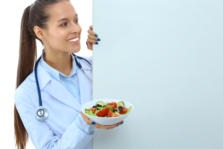 Portrait of a beautiful woman doctor holding a plate with fresh vegetables standing near blankの写真素材