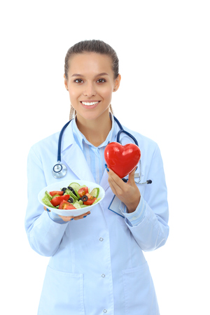Portrait of a beautiful woman doctor holding a plate with fresh vegetables and red heartの写真素材