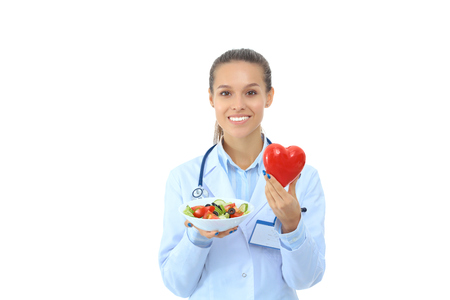 Portrait of a beautiful woman doctor holding a plate with fresh vegetables and red heartの写真素材