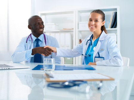 Two happy smiling young medical people handshaking at officeの写真素材