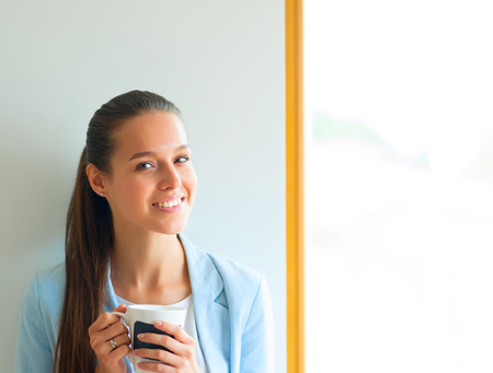 Attractive woman sitting at desk in office, working with laptop , having takeaway coffee.の写真素材