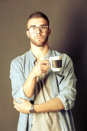 Portrait of a handsome young man standing and holding a cup of coffee in his handsの写真素材