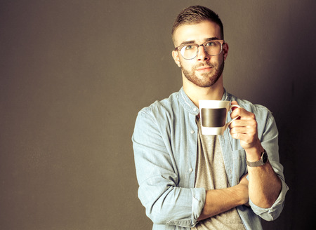 Portrait of a handsome young man standing and holding a cup of coffee in his handsの写真素材