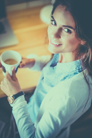 Portrait of relaxed young woman sitting at her desk holding cup of coffeeの写真素材