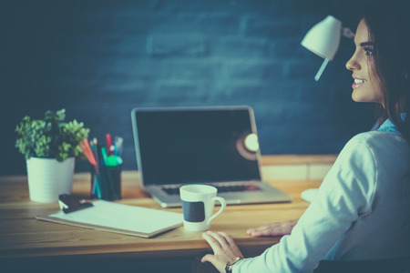 Portrait of relaxed young woman sitting at her desk holding cup of coffeeの写真素材