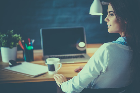 Portrait of relaxed young woman sitting at her desk holding cup of coffeeの写真素材