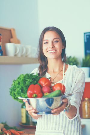 Smiling young woman holding vegetables standing in kitchen.の写真素材