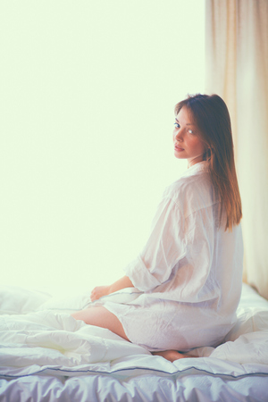 Young woman holding a pillow while sitting on her bed.の写真素材