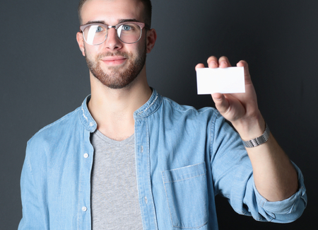 Young man holding a credit card standing on gray background.の写真素材
