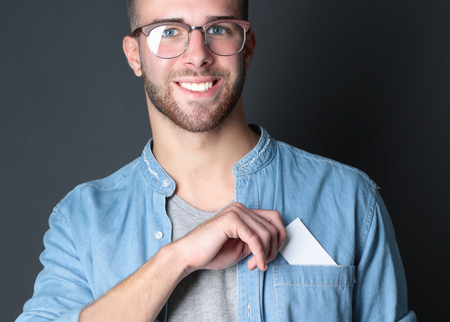 Young man holding a credit card standing on gray backgroundの写真素材