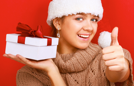A smiling woman on santa hat with christmas gifts and showing ok, isolated on red background.の写真素材