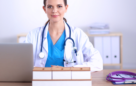 Beautiful young smiling female doctor sitting at the desk and writing.の写真素材