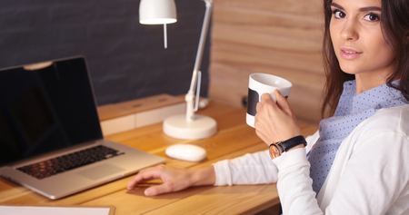Portrait of relaxed young woman sitting at her desk holding cup of coffeeの写真素材