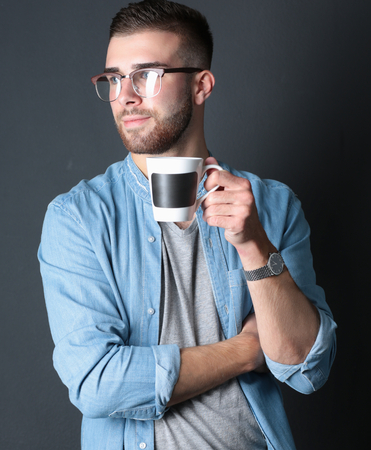 Portrait of a handsome young man standing and holding a cup of coffee in his handsの写真素材