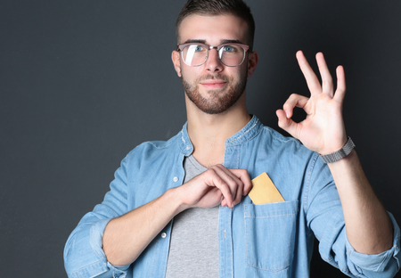 Young man holding a credit card standing on gray backgroundの写真素材