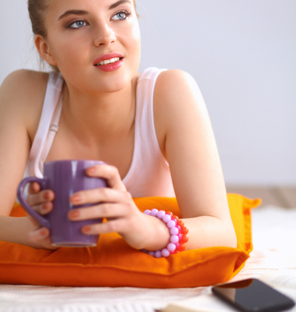 Smiling young woman lying on a white floor with pillow.の写真素材